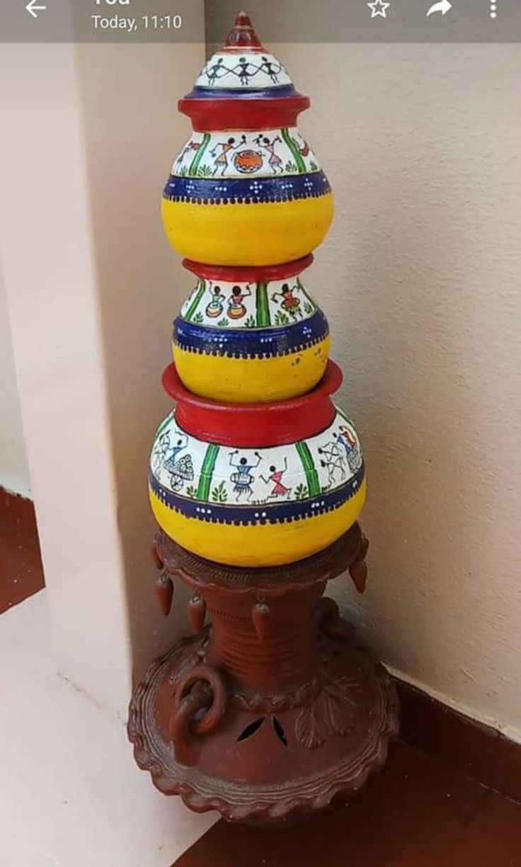 a colorfully painted vase sitting on top of a wooden stand next to a wall