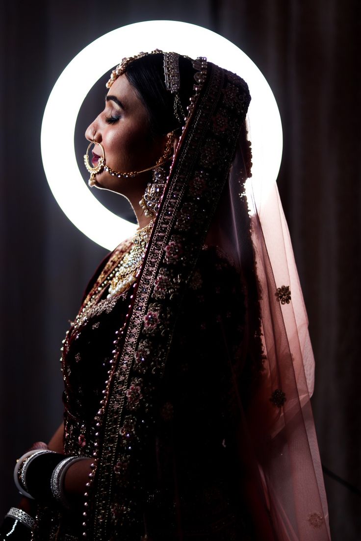 a woman wearing a veil and jewelry in front of a white circle with lights behind her