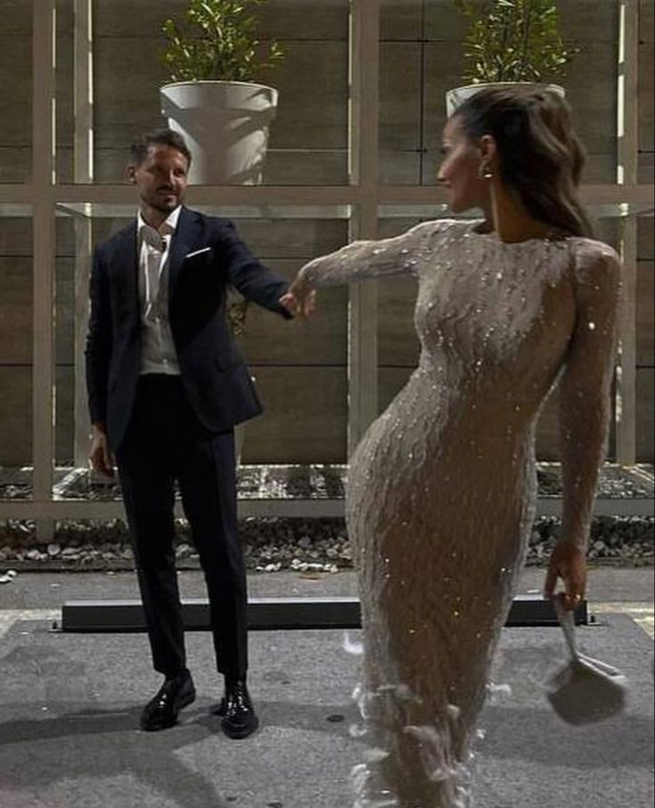 a man in a suit and tie shaking hands with a woman in a white dress