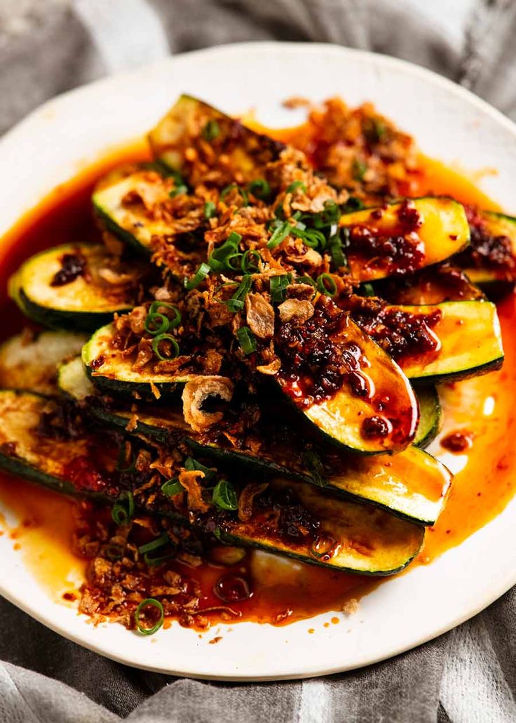 a white plate topped with zucchini covered in sauce and garnished with herbs