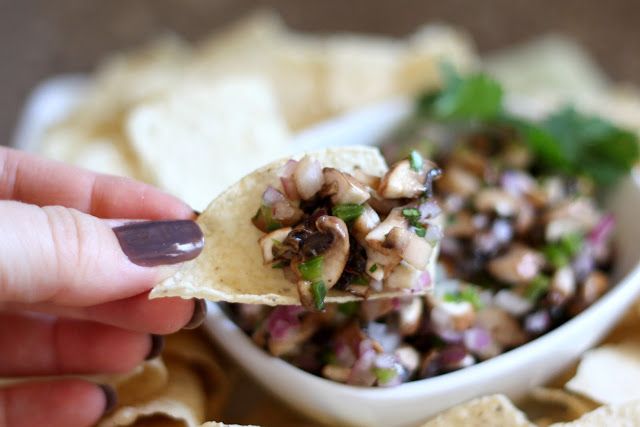 a hand holding a tortilla chip with black olives and mushrooms in it