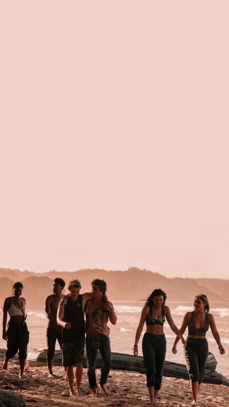 a group of people walking on top of a sandy beach next to the ocean with surfboards