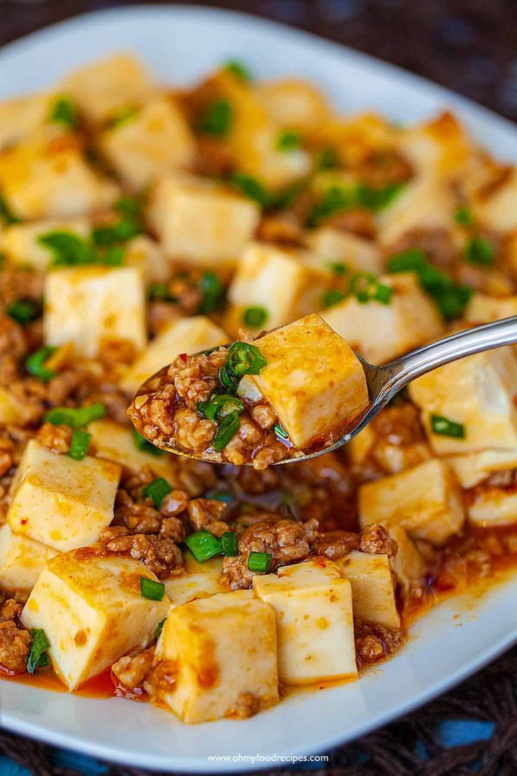 a white plate topped with tofu covered in sauce and garnished with green onions