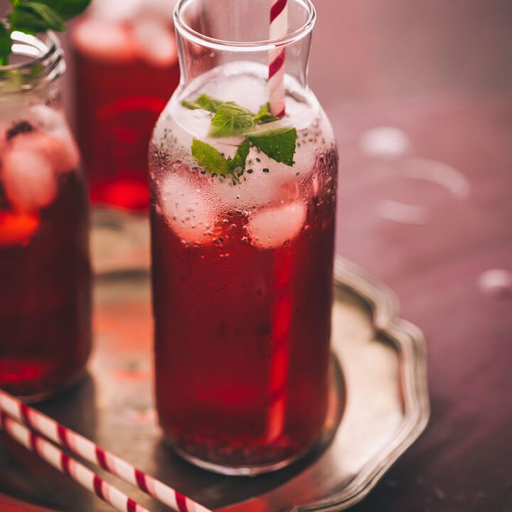 two glasses filled with red liquid and mint garnish on a tray next to a straw