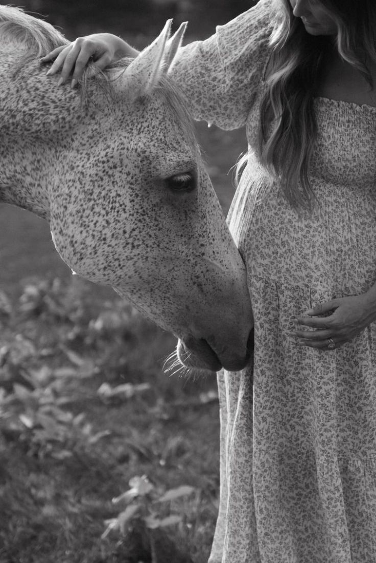 a pregnant woman standing next to a horse