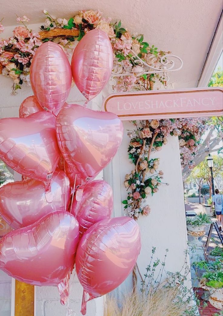 a bunch of pink heart shaped balloons hanging from the side of a building