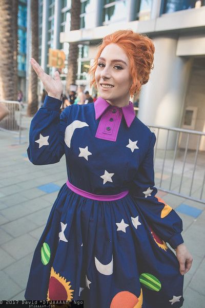 a woman with red hair wearing a dress and holding her hand up in the air