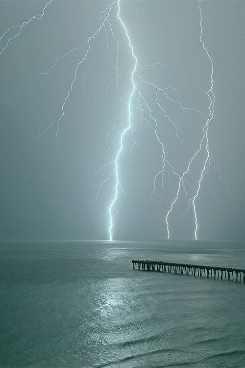 two lightning strikes over the ocean near a pier