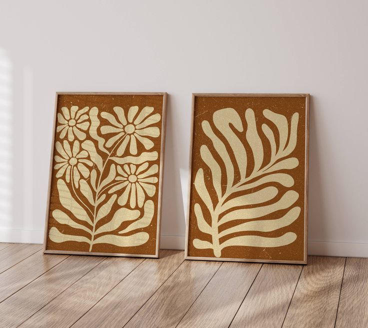 two brown and white paintings sitting on top of a wooden floor