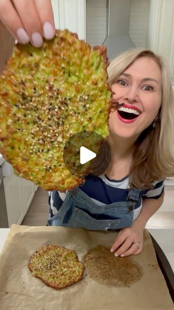 a woman holding up a pizza on top of a wooden cutting board next to an uncooked pizza