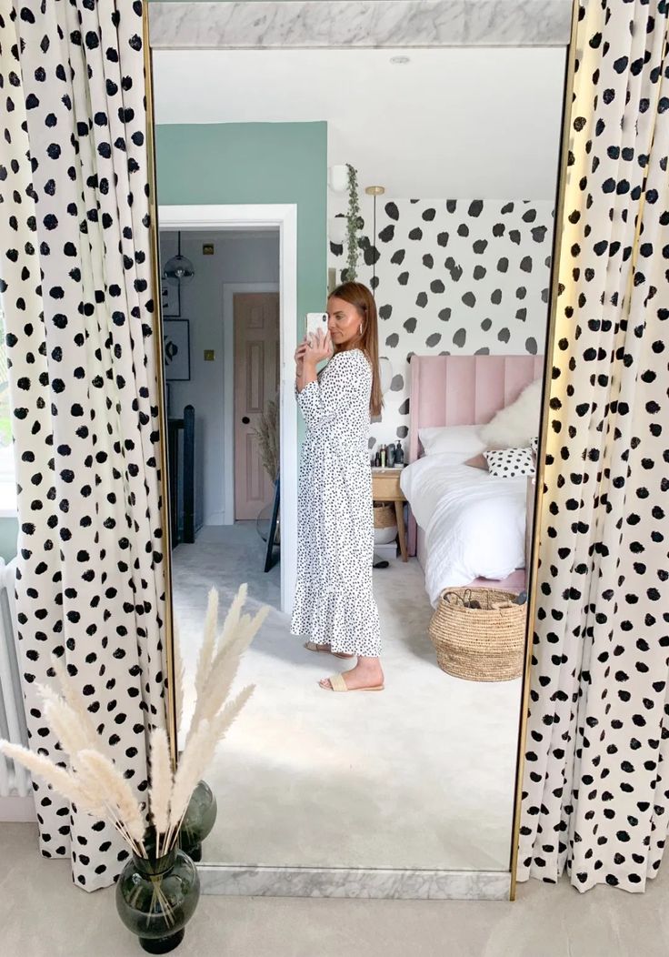 a woman standing in front of a mirror with polka dots on the walls and curtains