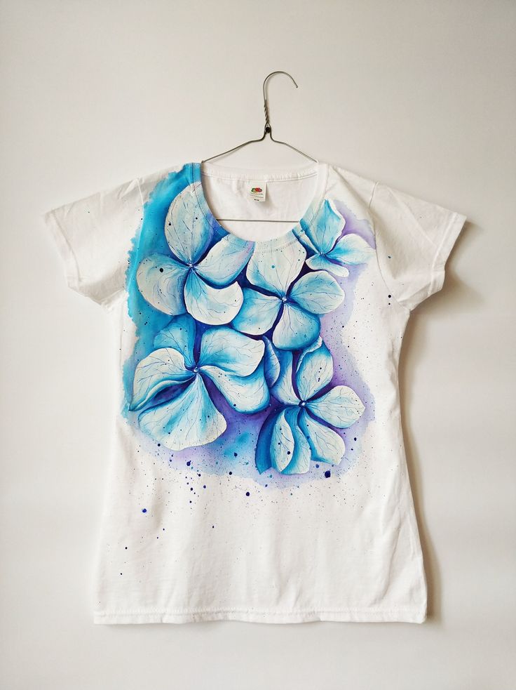 a white t - shirt with blue flowers painted on the front and back, hanging from a hanger