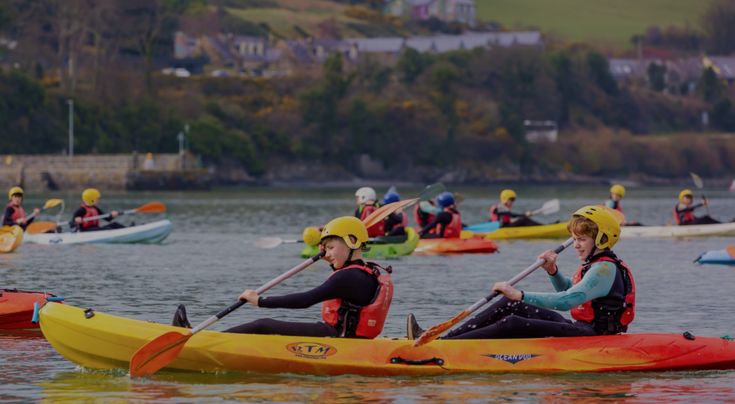 several people in kayaks paddling on the water with trees in the background and houses in the distance