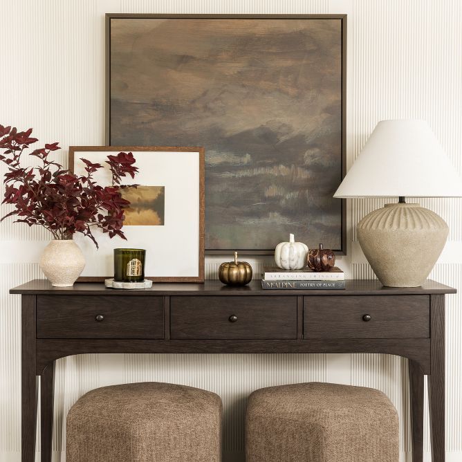 a console table with two stools and a painting on the wall