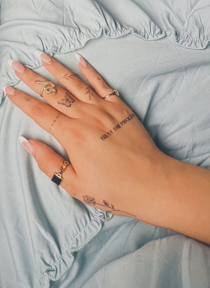 a woman's hand with tattoos on it laying on a blue bed sheet and pillows