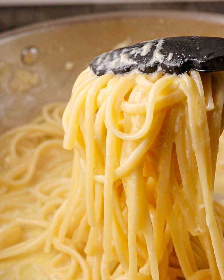 a spoon full of pasta being held up by someone's hand in a skillet