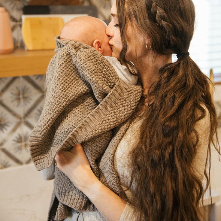 a woman holding a baby in her arms and kissing it's face with both hands