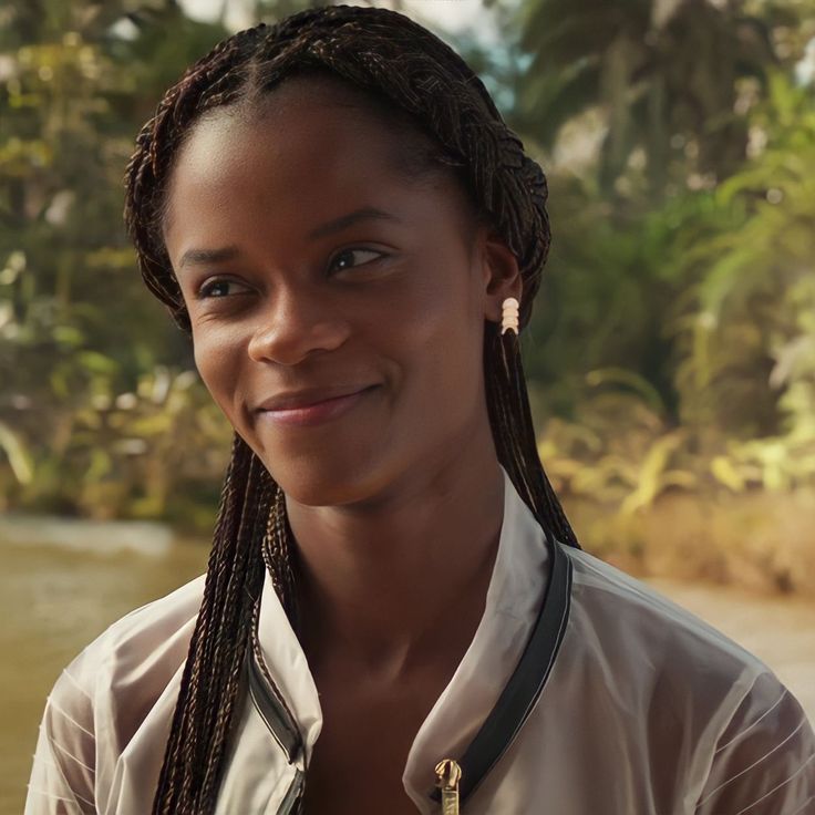 a woman with braids standing in front of a body of water and smiling at the camera