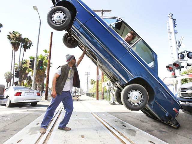 a man standing next to a blue car that is upside down