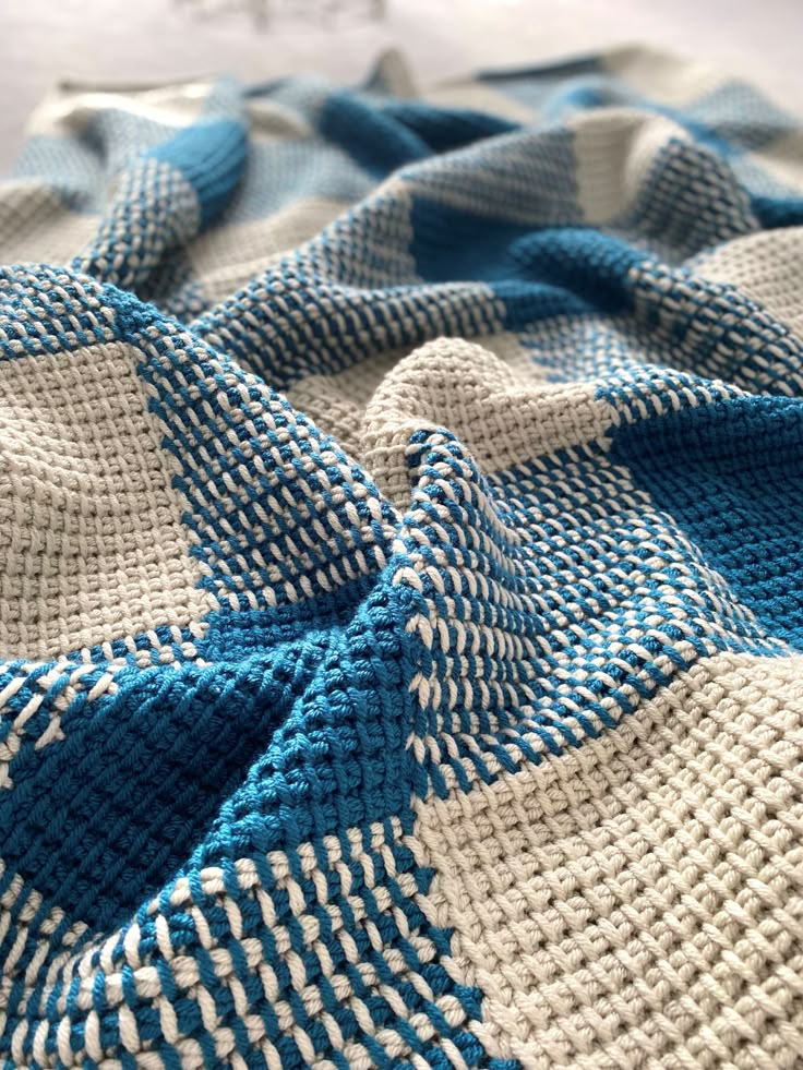 a blue and white knitted blanket laying on top of a bed