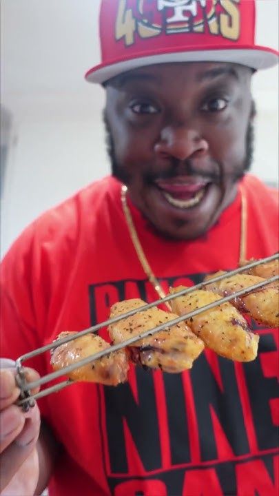 a man in a red shirt is holding some chicken skewers