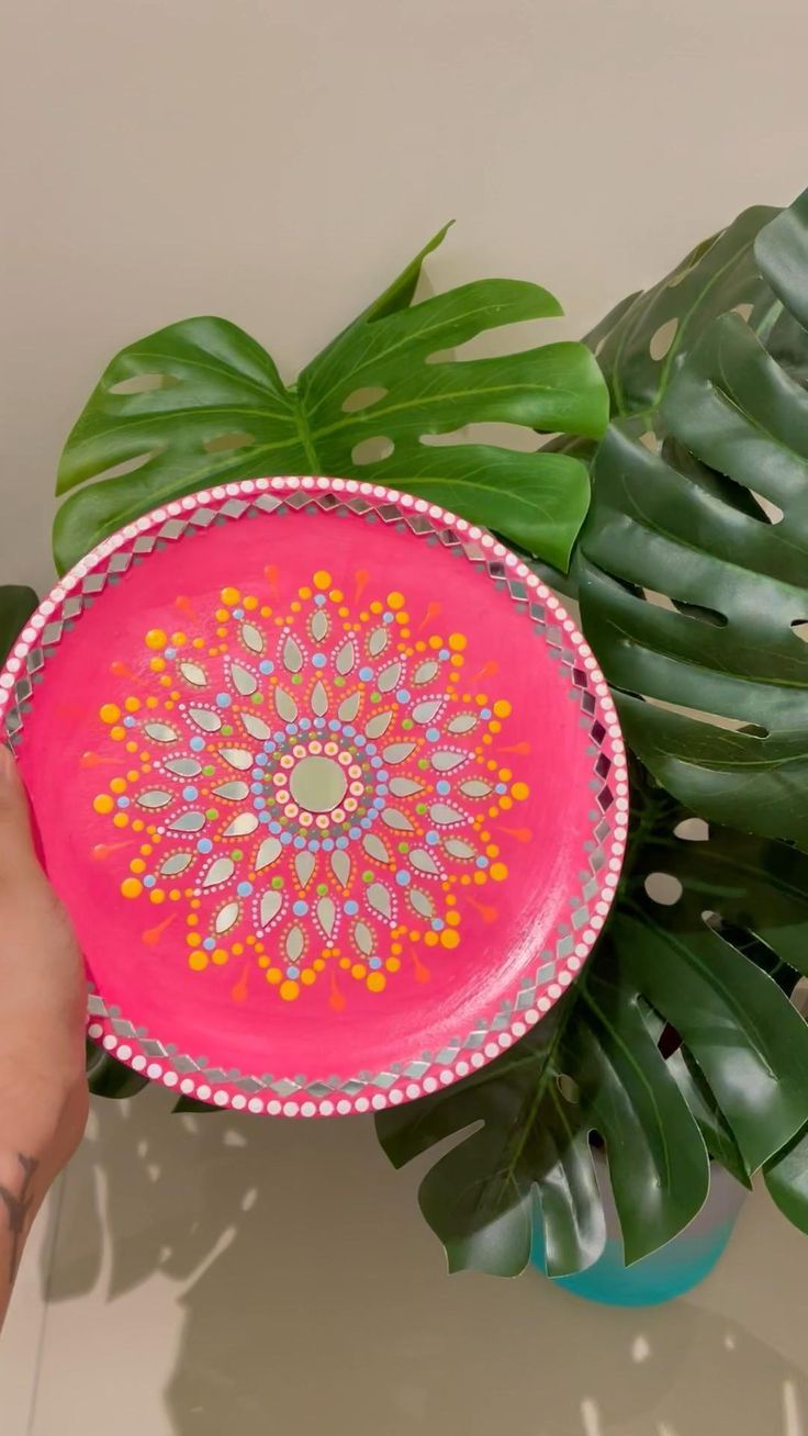 a person holding a pink plate with an intricate design on it next to a plant