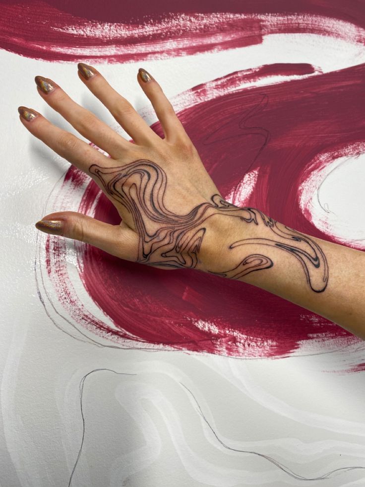 a woman's hand with a tattoo on her left arm and red paint splattered in the background