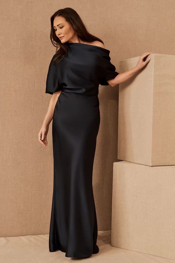 a woman in a black dress leaning against a wall with her hand on the side