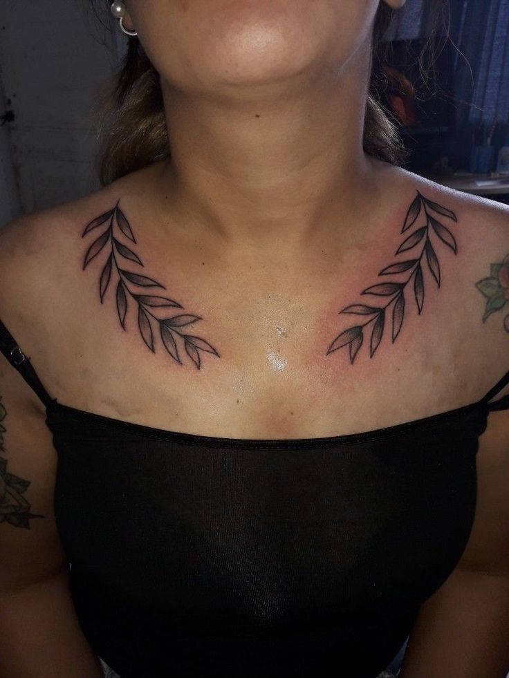 a woman with tattoos on her chest is looking up at the sky and has an olive branch tattoo on her chest