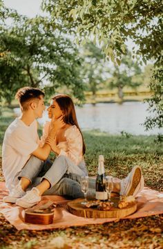 a man and woman are sitting on a blanket in the grass near a river with bottles