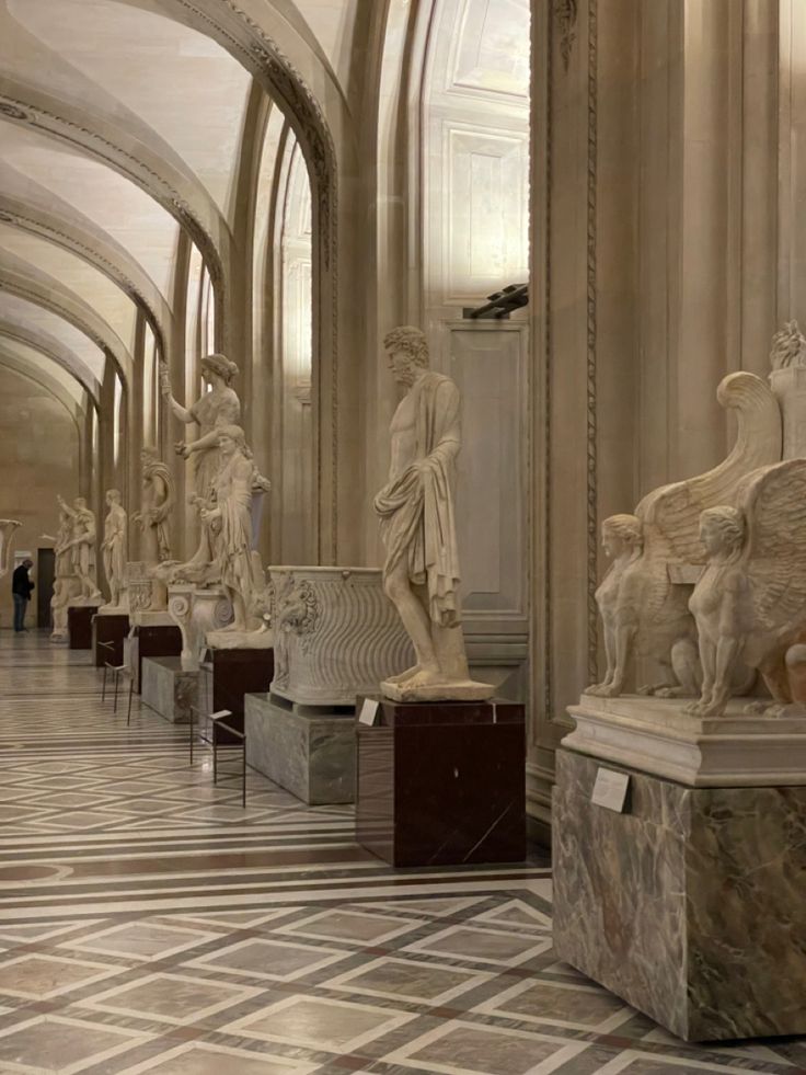 many statues are lined up in the middle of a room with marble floors and walls