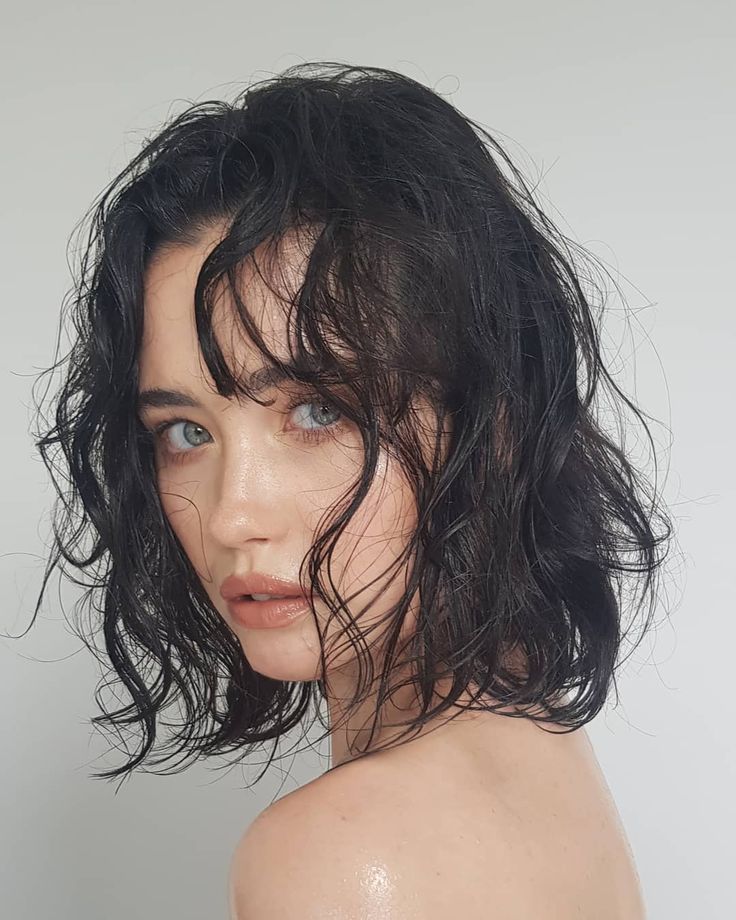 a woman with wet hair and blue eyes posing for the camera in front of a white background