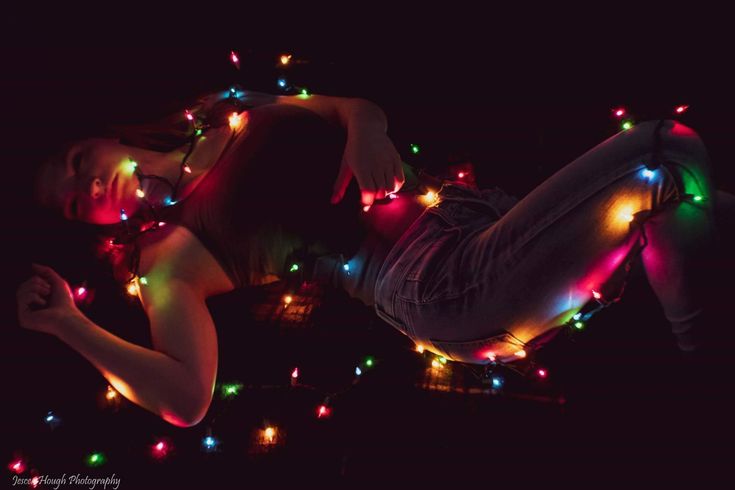 a woman laying on the ground with christmas lights all over her body and arms around her neck