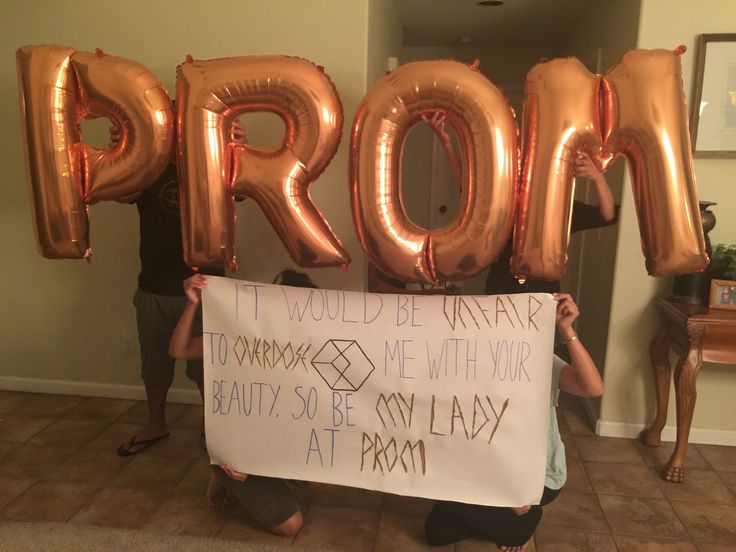 a person holding up a sign that says prom and balloons in the shape of letters