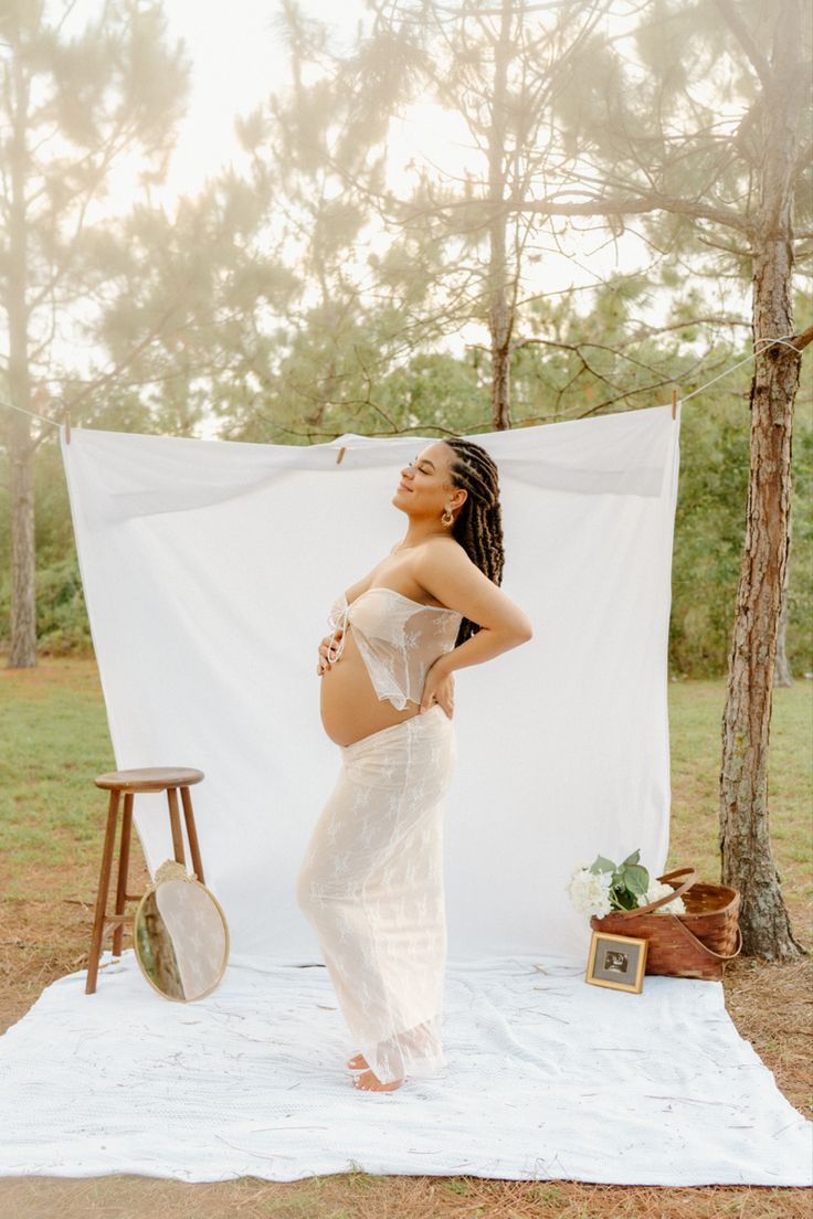 a pregnant woman standing on a blanket in front of a white backdrop holding a tennis racket