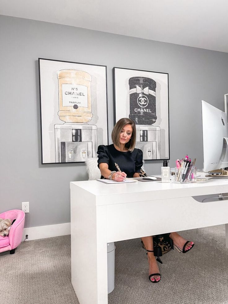 a woman sitting at a desk in front of a computer monitor and writing on a notepad