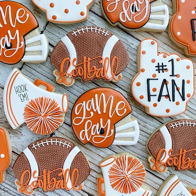 some decorated cookies that say football and game day are on a wooden table with orange accents