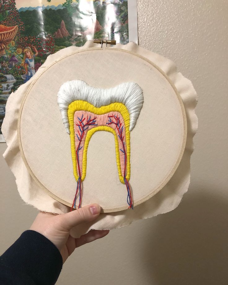 someone is holding up a embroidery art piece with a tooth on it and blood vessels running through the teeth