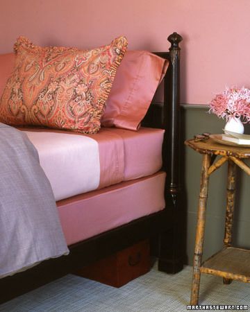 a bed with pink sheets and pillows next to a small wooden table in front of it