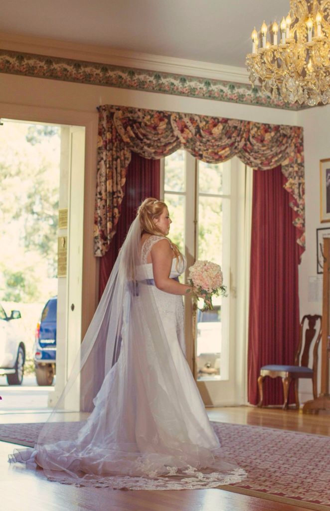 a woman in a wedding dress is standing near a chandelier and holding a bouquet