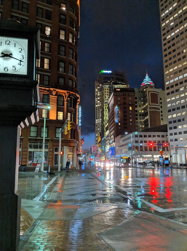 a city street at night with rain on the ground and buildings in the backround