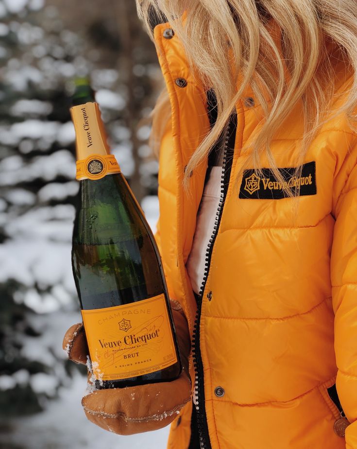 a woman holding a bottle of wine in her hand and wearing a yellow jacket with the words veuve closquet on it