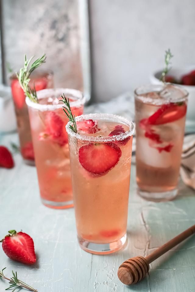 three glasses filled with ice and strawberries on top of a blue table next to utensils