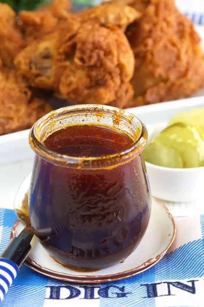 a glass jar filled with liquid sitting on top of a plate next to some fried chicken