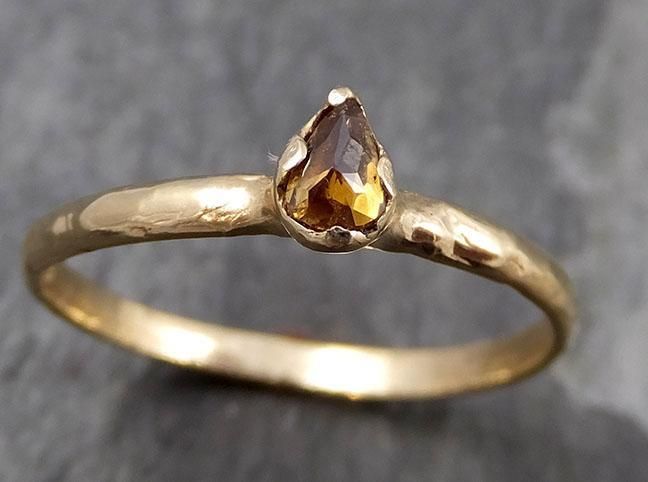 a yellow gold ring with a pear shaped brown diamond in the center, sitting on a gray surface