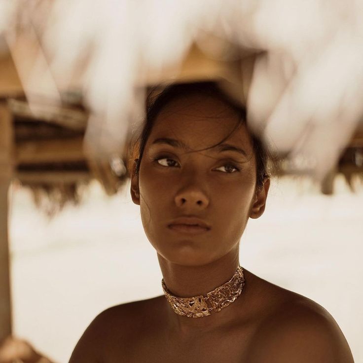 a woman wearing a necklace and choker standing under an umbrella on the beach with her eyes closed