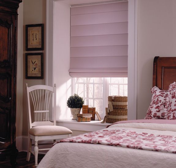 a bedroom with pink roman shades in the window and bedding on the other side