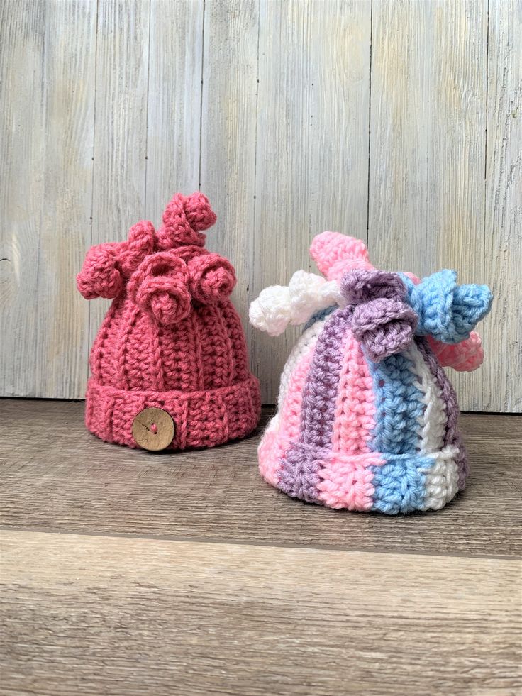 two crocheted hats sitting next to each other on a wooden surface with wood planks behind them