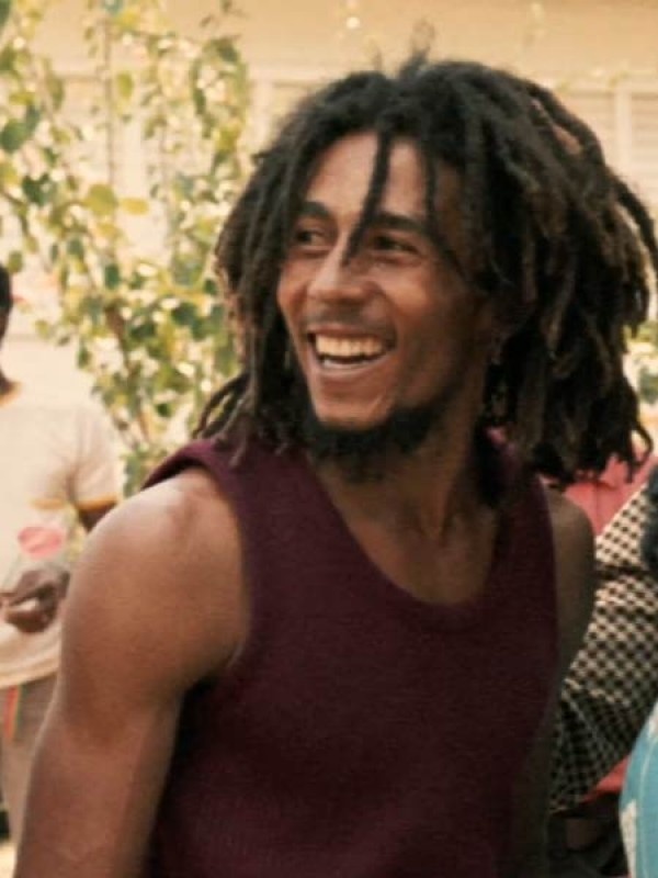 a man with dreadlocks smiles at the camera while standing in front of other people