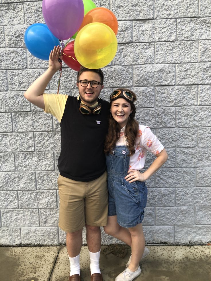 a man and woman standing next to each other with balloons on their heads in front of a brick wall